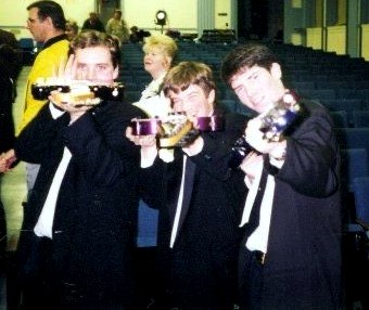 Three young guitarists in suits holding up their guitars