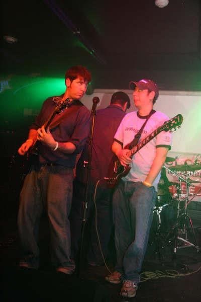 Two guitarists playing on a stage under green lights